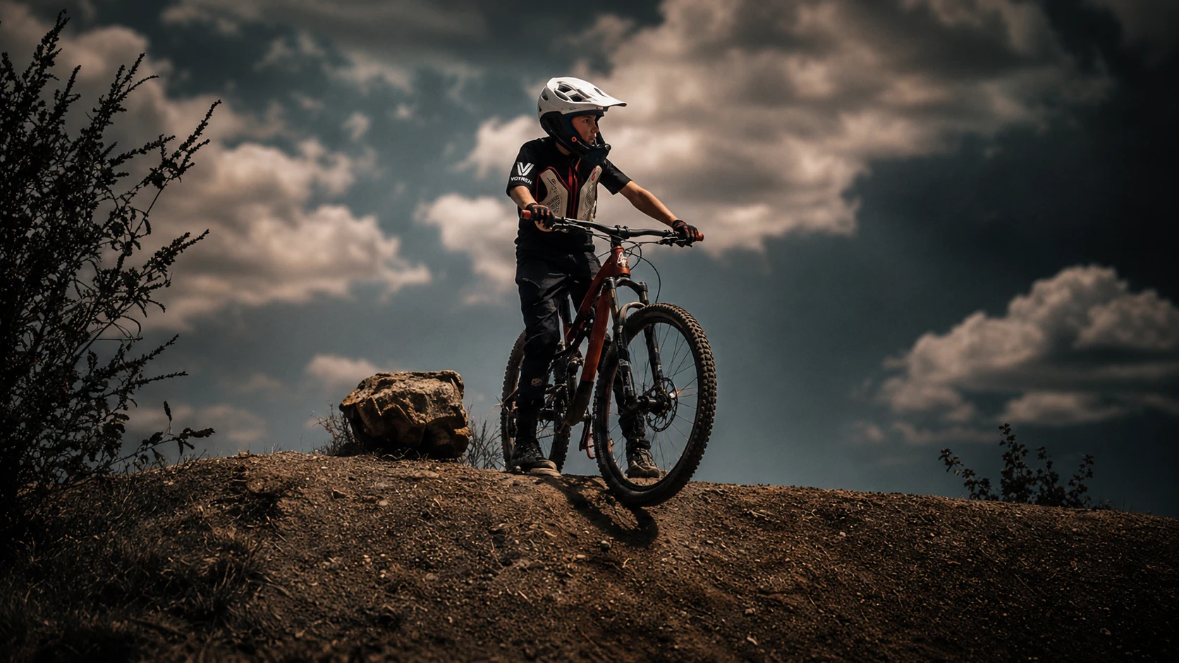VOYREN mountain biker on a dirt ridge under dark clouds